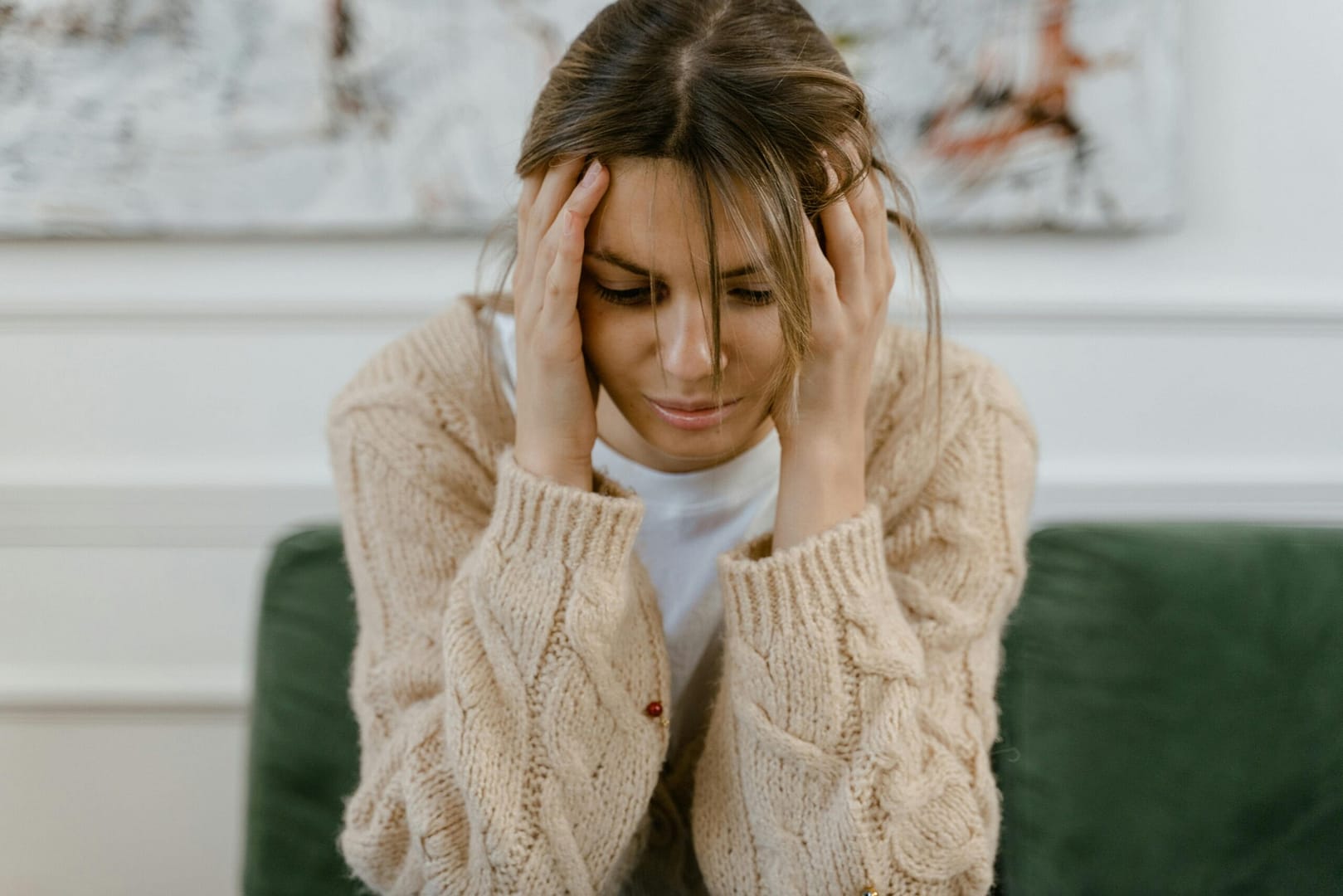 A woman sitting on a sofa holding her head, expressing stress and frustration indoors.