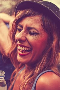 Smiling woman enjoying a fun nightclub party, wearing glitter and trendy hat.