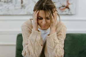 A woman sitting on a sofa holding her head, expressing stress and frustration indoors.