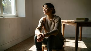 A person sitting in a quiet room, appearing calm and reflective with soft natural light streaming through a window.