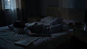 A person resting in a quiet bedroom, with a glass of water and a phone on silent on the nightstand, suggesting a need for rest and recovery.