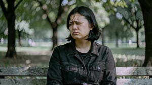 A person sitting on a wooden bench in a quiet park, showing a contemplative expression with a peaceful environment around them.